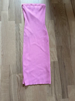 Rosa ribbad tubklänning från NA-KD - Säljer en rosa ribbad tubklänning från NA-KD i storlek XXS. Klänningen är figurnära och har en slits nertill. Perfekt för dig som gillar en enkel men snygg look med lite edge. Väldigt stretchig.
