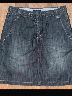 Marc O’Polo storlek 34, Mörkblå jeanskjol med snörning - Snygg mörkblå jeanskjol från Marc O'Polo med snörning i midjan och praktiska fickor fram. Kjolen har bälteshällor och klassisk jeanslook, perfekt för en avslappnad stil.