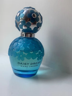 Marc Jacobs Daisy Dream parfym 50ml - Daisy Dream från Marc Jacobs är en parfym i en snygg blå glasflaska med blommönster och silverdetaljer. Flaskan har en rund form och locket är dekorerat med blå blommor. Perfekt för dig som gillar fräscha och blommiga dofter. Ca 75-80% kvar