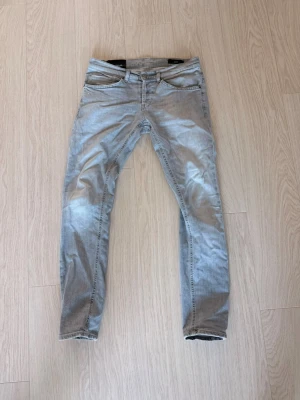 Ljusgrå Dondup Jeans  - Snygga ljusgrå Dondup jeans med klassisk femficksdesign och dragkedjegylf. Jeansen har en smal passform och är tillverkade i ett mjukt denimtyg som ger en skön känsla. Perfekta för en avslappnad och trendig stil. Jeansen är knappt använda och i storlek 31