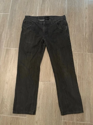 Svarta raka jeans med fickor - Snygga svarta jeans med rak passform och klassiska fem fickor, varav bakfickorna har lock och knapp. Jeansen har bälteshällor och stängs med dragkedja och knapp. Perfekta till en avslappnad stil. Vid intresse skriv privat för mer info om passform,bilder och storlek. Priset är inte hugget i sten!
