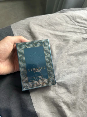 Versace Eros Eau de Parfum 100ml - Versace Eros Eau de Parfum i 100 ml storlek. Förpackningen är mörkblå med gulddetaljer och har det klassiska Versace-mönstret samt Medusa-huvudet på framsidan. Lyxig och elegant design som verkligen sticker ut i parfymhyllan.