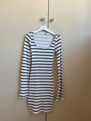 Randig ribbad klänning med lång ärm - Snygg kort ribbad klänning med svartvita horisontella ränder och lång ärm. Klänningen har en rundad, djup ringning och sitter figurnära. Perfekt för dig som gillar en enkel men trendig stil.