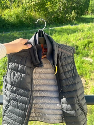 Svart dunväst från Parajumpers - Snygg svart dunväst från Parajumpers med quiltad design och hög krage. Västen har dragkedja framtill, två sidofickor med dragkedja och en gul detalj vid halsen. Perfekt för lager-på-lager och håller dig varm under kyliga dagar. Priset kan diskuteras 😁