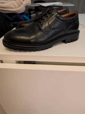 Svarta loafers i läder med grov sula - Stilrena svarta loafers i äkta läder med robust, räfflad gummisula och klassisk snörning. Skorna har en tidlös design med rundad tå och diskreta sömmar. Perfekta för dig som vill ha en snygg och bekväm sko till vardagslooken. Sjukt bekväma!!