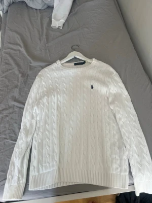 Vit kabelstickad tröja Polo Ralph Lauren - Säljer en klassisk vit kabelstickad tröja från Polo Ralph Lauren. Tröjan är lite sönder vid en av  axlarna, men annars i perfekt kondition.