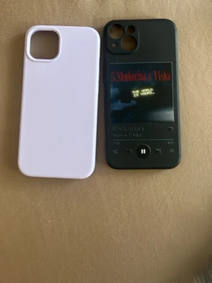 Två mobilskal, lila & svart design - Säljer två mobilskal till iPhone. Ett är lila och har en enkel, stilren design. Det andra är svart med ett tryck som ser ut som en musikspelare med text och knappar. Båda är gjorda i mjukt plastmaterial och har öppningar för kamera och knappar.