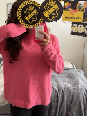 Rosa stickad tröja - Mysig rosa stickad tröja med rund hals och långa ärmar. Tröjan har en enkel, avslappnad passform och ribbade muddar vid ärmslut och nederkant. Perfekt för att hålla värmen under kyliga dagar.