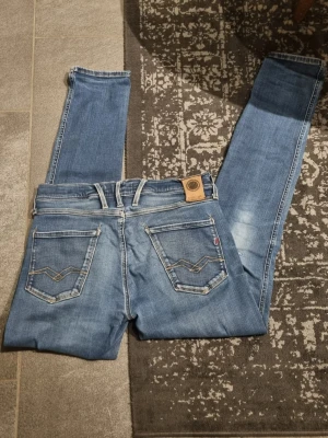 Replay Anbass - Säljer ett par klassiska blå jeans från Replay med raka ben och snygga detaljer på bakfickorna. Jeansen har fem fickor, ljus tvätt och kontrastsömmar. Perfekta för dig som gillar en tidlös och avslappnad stil. Skicka dm vid eventuella frågor! ( små slitningar runt jeansen )