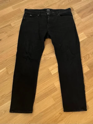 Svarta jeans från BOSS - Snygga svarta jeans från BOSS med klassisk femficksdesign och raka ben. Jeansen har diskreta sömmar och en stilren look som passar till det mesta. Materialet är mjukt och stretchigt för extra komfort. Stod något om cashmere design som då menar att byxan ska vara lika skön som cashmere inuti. Skönaste byxorna jag ägt tyvärr passar dom inte så jag måste göra mig av med dom. Passar som en 36a.