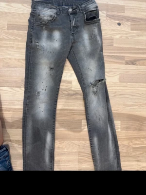 Dsquared2 jeans  - Säljer ett par grå jeans med slitningar och hål på flera ställen. Jeansen har en tvättad look och klassisk femficksmodell. Perfekta för dig som gillar en edgy och avslappnad stil.