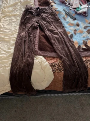Bruna mjukisbyxor i velour - Mysiga bruna mjukisbyxor i velour med bred resår i midjan och dragsko. Byxorna har raka ben och bakfickor med lock och knappdetaljer. Perfekta för en avslappnad och trendig look.