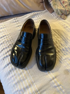 Svarta Tabi loafers - Svarta tabi loafers från Maison Margiela. Köpta i Milano butiken 2024, max använda typ 25ggr. Finns nästan aldrig i dehär storlekarna i butik brukar vara svåra att hitta. Har original låda och allt och om ni kollar på min Grailed kan ni se att allt är äkta och att de är verified. Sjuk sko, värd varenda krona, säljer för att jag behöver pengar och ska byta till en annan tabi model. Storlek 45 🙏🙏 Har fler bilder om det önskas. 