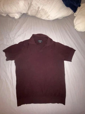 Vinröd stickad pikétröja. - Snygg vinröd stickad pikétröja med korta ärmar och klassisk krage. Tröjan har ribbstickad nederkant och är tillverkad i mjukt material. Den är tyvärr för liten för mig. Den har ett litet hål på höger bröstkorg. Det är ett lite finare/ dyrare märke. Ny pris 400kr, storlek S