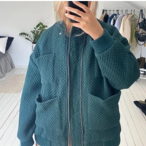 Grön quiltad bomberjacka - Snygg grön quiltad bomberjacka med dragkedja framtill och stora fickor. Jackan har ribbade muddar vid ärmslut och nederkant samt en cool oversized passform. Perfekt för dig som vill ha en trendig och bekväm look.