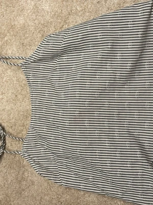 Randig linnetopp med broderad kant - Snygg randig linnetopp med tunna axelband och broderad, vågig kant nertill. Toppen har svartvita ränder och små broderade detaljer i tyget. Perfekt för en somrig och avslappnad look. Helt ny aldrig använd.