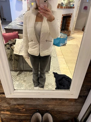 Vit pufferjacka med fuskpäls - Säljer en snygg vit pufferjacka med dragkedja framtill och två snedställda fickor med dragkedja. Jackan har en hög krage med fuskpäls och quiltad design som ger en modern look. Perfekt för kalla dagar.