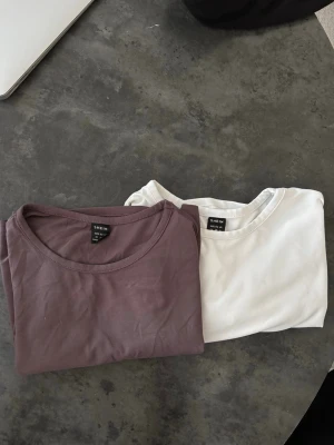 Två basic t-shirts från SHEIN - Säljer två basic t-shirts från SHEIN i storlek M. Ena är vit och den andra är brunlila. Båda har rund halsringning och korta ärmar. Perfekta att matcha med jeans eller kjol för en enkel och clean look. Skims material på båda, 30:- för 1 och 2 för 50:-