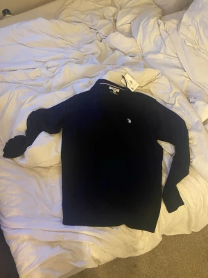 Marinblå merinoulltröja U.S. Polo Assn. - Snygg marinblå stickad tröja från U.S. Polo Assn. i mjuk merinoull. Tröjan har rund halsringning, diskret logga broderad på bröstet och ribbade muddar vid ärmslut och nederkant. Perfekt för dig som gillar klassisk och stilren look.