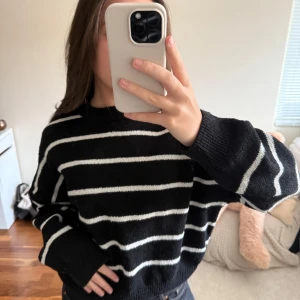 Svartvit randig stickad tröja - Säljer en svart stickad tröja med vita horisontella ränder. Tröjan har rund halsringning, långa ärmar och en avslappnad passform. Perfekt för dig som gillar en enkel men stilren look.