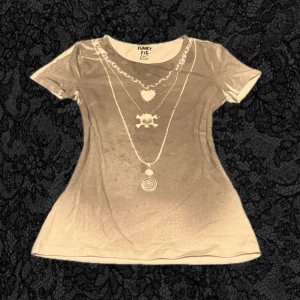Grå t-shirt med tryck från Funky Fig - Cool grå t-shirt från Funky Fig med tryck av kedjor och smycken på framsidan. T-shirten har rund halsringning och korta ärmar. Materialet känns mjukt och stretchigt, perfekt för en unik och edgy stil.