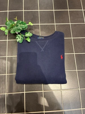 sweatshirt från Polo Ralph Lauren(160 cm) - Klassisk mörkblå sweatshirt från Polo Ralph Lauren med rund halsringning och den ikoniska röda logon broderad på bröstet. Tröjan har ribbade muddar vid ärmslut och nederkant. Perfekt för en clean och stilren look.