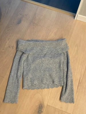 Stickad tröja. Grå off shoulder - Säljer en ribbstickad grå off shoulder-tröja med volangkant upptill och nedtill. Tröjan har långa ärmar och en mjuk, stretchig passform. Perfekt för dig som vill ha en trendig och bekväm look. Köpt på Walmart i usa 🇺🇸 