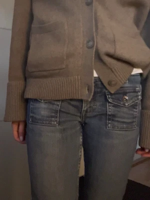 Blå bootcut jeans med fickdetaljer - Snygga blå bootcut jeans fickor framtill och baktill som har lock och knapp. Jeansen har en klassisk femficksmodell och är tillverkade i denim med en tvättad look. Älskar dessa! De är ca 36 cm rakt över i midjan och ca 79 cm i innerbenslängd. Skriv gärna vid frågor!💕