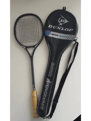 Dunlop Turbo Boron Squashracket  - Klassiskt svart squashracket från Dunlop, modell Turbo Boron, med oversize ram i borongrafit och gul grepptejp. Medföljer svart fodral med axelrem och tydlig Dunlop-logga. Perfekt för dig som gillar retro sportprylar. Har även använts till badminton och tennis. Fint skick!!