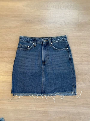 Mörkblå jeanskjol med rå kant från HM - Supersnygg trendig mörkblå jeanskjol i kort modell med rå, fransig kant nedtill. Säljer då den är lite för liten på mig