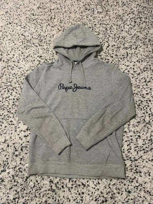 Grå hoodie från Pepe Jeans - Snygg grå hoodie från Pepe Jeans med broderad logga på bröstet. Tillverkad i mjukt bomullsmaterial, perfekt för en avslappnad stil.