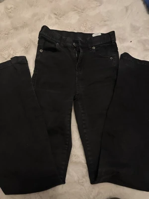 Svarta ripped jeans med hål på knäna - Säljer ett par svarta jeans med skinny fit och slitna hål på båda knäna. Jeansen har klassisk femficksmodell, dragkedja och knapp i midjan. Perfekta för dig som gillar en edgy och avslappnad stil.