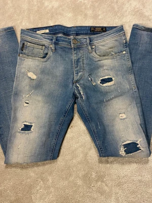 Jack n Jones jeans  - Säljer  Jack n Jones jeans med skön tvätt o feta slitningar. Jeansen är i storleken W31 L32. Modellen är Slimfit/Glenn. De är i bra skick förutom slitningen under gylfen som man ser vid bild 1. Skriv för frågor! 
