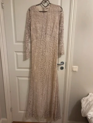 Lång ljus spetsklänning med struktur - Elegant långklänning i ljus beige ton med vackert strukturerat spetsmönster. Klänningen har lång ärm och rund halsringning, samt en figurnära passform upptill som faller snyggt nedåt. Perfekt för dig som vill ha en stilren och romantisk look. Kolla min profil för fler plagg! 🥰