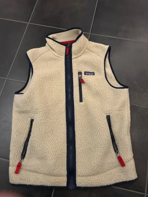 Beige Patagonia fleeceväst - Säljer en beige fleeceväst från Patagonia med marinblå detaljer och röda dragkedjor. Ny pris runt 1500 mitt pris 1000