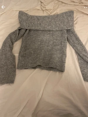 Grå off shoulder stickad tröja - Trendig grå ribbstickad tröja med bred off shoulder-krage och långa ärmar. Perfekt för dig som gillar en avslappnad men ändå snygg stil. Materialet ser mjukt och bekvämt ut, och modellen är något boxig.