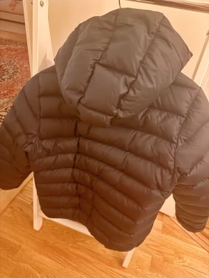 Svart dunjacka med huva från Colmar - Svart dunjacka från Colmar Originals med quiltad design och stor huva. Jackan är en lätt puffar och är perfekt för kalla vinterdagar. Passar  dig som är ca 150 - 165 cm.  Använd men gott skick. Inga märken eller hål. 