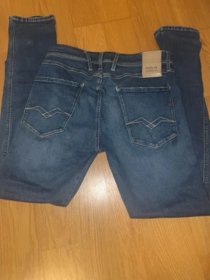 Replay Anbass slim fit jeans blå - Säljer ett par snygga blå Replay Anbass jeans i slim fit-modell. Klassisk femficksdesign med coola sömmar på bakfickorna och läderpatch med logga bak i midjan. Med en slittning. Jeansen är tillverkade i mjukt denimtyg och har en modern passform. W31 L32