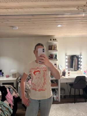 Vit t-shirt med rött coolt tryck - Snygg beige T-shirt med rött grafiskt tryck framtill och rund hals. T-shirten har korta ärmar och en avslappnad passform, perfekt till jeans eller shorts. Trycket har en vintagekänsla och ger en cool retrostil.