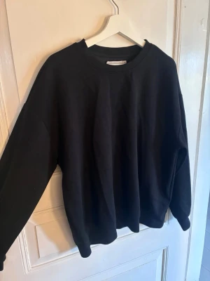 Svart basic sweatshirt Lager 157 - En enkel svart sweatshirt från Lager 157 i storlek M. Tröjan har rund halsringning, långa ärmar och en avslappnad passform. Tillverkad i mjukt bomullsmaterial som är skönt mot huden. Perfekt för dig som gillar minimalistisk stil.