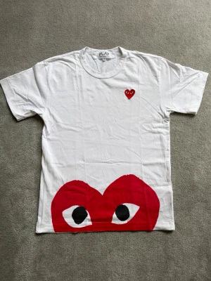 Vit Comme des Garçons Play t-shirt - Säljer en vit Comme des Garçons Play t-shirt med tryck då den bara legat runt i min garderob och det är dags för den att få nytt liv! T-shirten har storlek M (passar S) men är som sagt lite mindre i storleken då CDG storlekar brukar sitta lite mindre. Fråga på om du undrar över något - svarar snabbt!