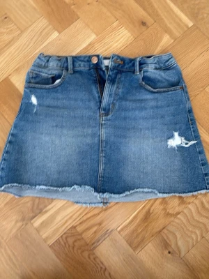 Blå jeanskjol med rå kant - Snygg blå jeanskjol i kort modell med slitna detaljer och rå kant nertill. Kjolen är justerbar i midjan och är luftig i tyget. Perfekt för en avslappnad och trendig look ☀️🤗. 