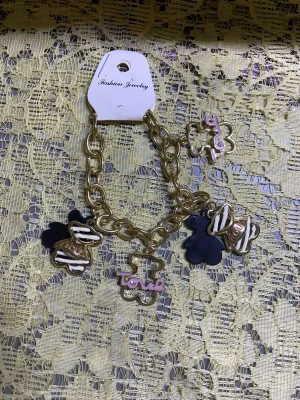 Guldigt armband med björnberlocker - Snyggt armband i guldfärgad metall med stora länkar och flera björnformade berlocker i svart, vitt och guld. Några berlocker har texten 'love' i rosa. Perfekt accessoar för dig som gillar lekfulla detaljer och trendiga smycken.