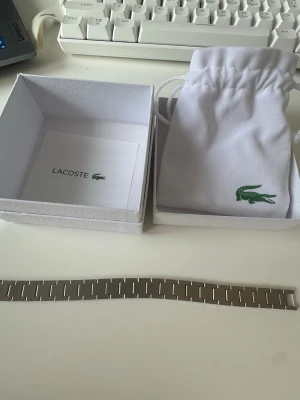 Lacoste - bracelet - Stilrent armband från Lacoste i silverfärgad metall med rektangulära länkar. Kommer med original ask och vit tygpåse med Lacoste-logga. Perfekt accessoar för dig som gillar minimalistisk och modern design.