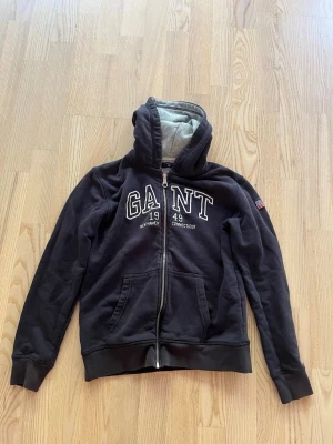 Marinblå zip hoodie från GANT - Snygg marinblå hoodie från GANT med dragkedja och vit brodyr på bröstet. Storlek 158/164.