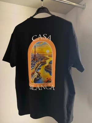 Casablanca tshirt - Svart t-shirt från Casablanca med färgstarkt tryck av en stadsscen på både bröstet och ryggen. T-shirten har rund hals och korta ärmar. Materialet är mjuk bomull och passformen är normal. Perfekt för dig som vill ha en unik och trendig look.