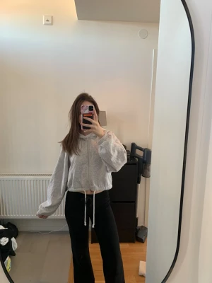 Grå croppad hoodie  - Säljer en ljusgrå croppad hoodie med snöre nertill där man kan dra åt.