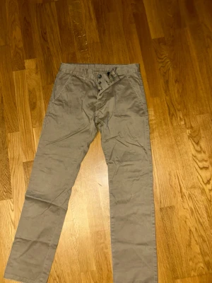 Beige chinos från Dr. Denim - Snygga beige chinos från Dr. Denim med raka ben och klassisk knappgylf. Tillverkade i mjuk bomull som ger en skön känsla hela dagen. Perfekta för dig som gillar en clean och enkel stil.