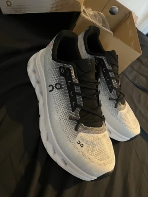  On cloud skor  - Snygga sneakers från On i vitt och svart med mesh-överdel för bra ventilation. Skorna har en chunky sula med tydliga dämpningsdetaljer och svarta snören. Perfekta för dig som gillar sportig och modern stil.