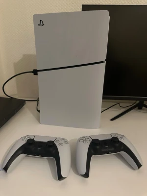 PlayStation 5 Digital Edition med 2 kontroller - Säljer en PlayStation 5 Digital Edition med 1TB lagring. Konsolen är vit med svart detalj och har en futuristisk, stilren design. Två matchande DualSense-kontroller i vitt och svart ingår. Perfekt för gaming i 4K och HDR. Originalkartong medföljer.